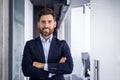 Portrait of a young successful businessman in a suit standing inside the office, crossing his arms on his chest Royalty Free Stock Photo