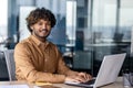 Portrait of young successful Indian man at workplace inside office, businessman smiling and looking at camera, man at work using Royalty Free Stock Photo