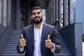 Portrait of young successful Muslim man businessman, lawyer standing near court building in suit, smiling and pointing