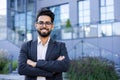 Portrait of a young successful and smiling Muslim male businessman standing outside an office building in a suit and Royalty Free Stock Photo