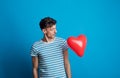 Portrait of a young man in a studio on a blue background, looking at red heart. Royalty Free Stock Photo
