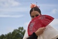 Portrait of young teenage girl in black dance dress, white shawl and pink carnations in her hair, dancing flamenco with a red fan Royalty Free Stock Photo