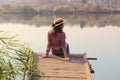 Portrait of a young teenage girl sitting on a wooden bridge near the river and looking to the side, back view. Royalty Free Stock Photo