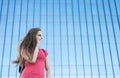 Portrait of young teenager brunette girl in coral t-shirt with long hair. girl on city talking on the smart phone. Glass building Royalty Free Stock Photo