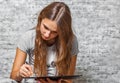 Young teenager brunette girl with long hair drawing with pencil on gray wall background