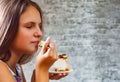 Young teenager brunette girl with long hair eating cake dessert on gray wall background Royalty Free Stock Photo