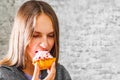 Young teenager brunette girl with long hair eating cream cake on gray wall background Royalty Free Stock Photo