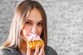 Young teenager brunette girl with long hair eating cream cake on gray wall background Royalty Free Stock Photo