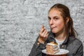 Young teenager brunette girl with long hair eating slice cake dessert on gray wall background Royalty Free Stock Photo
