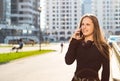 Portrait of young teenager brunette girl with long hair. girl on city in black dress talking on the smart phone in the street in a Royalty Free Stock Photo