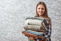Portrait of young teenager brunette girl with long hair holding in hands Stack of cozy knitted sweaters on gray wall background