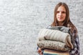 Portrait of young teenager brunette girl with long hair holding in hands Stack of cozy knitted sweaters on gray wall background