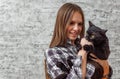 Portrait of young teenager brunette girl with long hair holding in her arms black cat on gray wall background Royalty Free Stock Photo