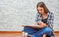 Portrait of young teenager brunette girl with long hair sitting on floor and drawing picture on gray wall background Royalty Free Stock Photo