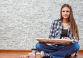 Portrait of young teenager brunette girl with long hair sitting on floor and drawing picture on gray wall background Royalty Free Stock Photo