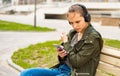 Portrait of young teenager brunette girl with long hair. young woman listening to music using mobile phone sitting on bench Royalty Free Stock Photo