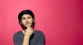 Portrait of young thinking man touching his chin, isolated on pink coral background. Royalty Free Stock Photo