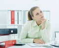 Portrait of young tired businesswoman sitting at the desk with a stack of folders.