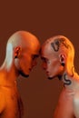 Portrait of young twin brothers with tattoos and piercings standing head to head, looking at each other isolated over