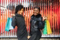 Portrait of young two african ladies friends standing over red wall and posing with shopping bags Royalty Free Stock Photo