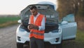 Portrait of young upset businessman staying on countryside road, using smartphone for calling help evacuator evacuating