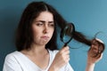 Portrait of a young upset Caucasian woman examining the tips of her hair through a magnifying glass. Blue background Royalty Free Stock Photo