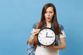 Portrait of young upset puzzled woman student in denim clothes with backpack hold alarm clock isolated on blue Royalty Free Stock Photo