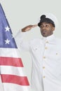 Portrait of a young US Navy officer saluting American flag over gray background Royalty Free Stock Photo