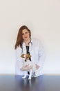 Portrait of a young veterinarian woman examining a cute small dog by using stethoscope, isolated on white background. Indoors Royalty Free Stock Photo