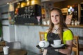 Portrait young waitress standing in cafe. girl the waiter holds in bunches a tray with utensils Royalty Free Stock Photo