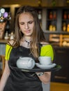 Portrait young waitress standing in cafe. girl the waiter holds in bunches a tray with utensils Royalty Free Stock Photo