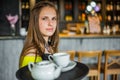 Portrait young waitress standing in cafe. girl the waiter holds in bunches a tray with utensils. Royalty Free Stock Photo