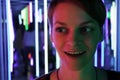 Portrait of a young woman with an amazed smile and wide open eyes in surprise, headshot in neon pink-green lighting, with crooked