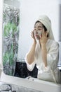 Portrait of a young woman applying a black cream face mask for skin in front of her bathroom mirror after a relaxing shower. Royalty Free Stock Photo