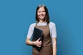 Portrait of young woman in apron holding laptop on blue background Royalty Free Stock Photo