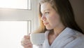 Closeup portrait of young woman in bathrobe looking out of the window and drinking coffee Royalty Free Stock Photo