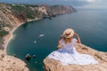 Portrait of a young woman on the beach by the sea, sitting with raised hands in a white dress and hat. Back photo Royalty Free Stock Photo