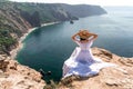 Portrait of a young woman on the beach by the sea, sitting with raised hands in a white dress and hat. Back photo Royalty Free Stock Photo