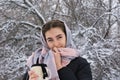 Portrait of  young woman with beautiful blue eyes. Lady on walk in  winter snowy forest drinks hot tea from mug and holds scarf Royalty Free Stock Photo