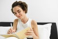 Portrait of young woman in bed, working or studying, writing in her journal, reading notebook notes, sharing thoughts