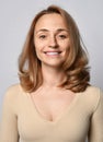 Portrait of young blonde woman in beige shirt with long sleeves with open friendly smile looking at camera