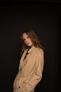 Portrait of young woman in black top and beige trench coat on black background