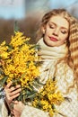 Portrait of a young woman with blond hair holding a bouquet of mimosa in her hands. Spring Royalty Free Stock Photo