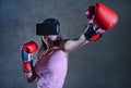 Portrait of young woman with boxing gloves playing video game using VR virtual reality goggles simulating boxer fighting 3D illusi