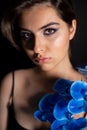 Portrait of young woman with bright blue eyeshadows, pink lips, covering shoulder with branch of blue orchid flower. Royalty Free Stock Photo