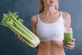 Portrait of a young woman with a bunch of celery in one hand and a glass of celery juice in the other. dark background, studio