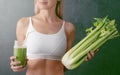 Portrait of a young woman with a bunch of celery in one hand and a glass of celery juice in the other. dark background, studio