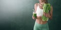 Portrait of a young woman with a bunch of celery in one hand and a glass of celery juice in the other. dark background, studio Royalty Free Stock Photo