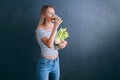 Portrait of a young woman with a bunch of celery in one hand and a glass of celery juice in the other. dark background, studio