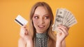 Portrait of a young woman choosing cash over the credit card. Close up shot isolated on the orange background Royalty Free Stock Photo